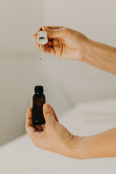 Close up of woman's hands holding a bottle of cosmetic serum with dropper.