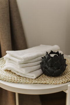 Minimalist still life of luxury spa essentials. White cotton towels with decorative candle on a table.