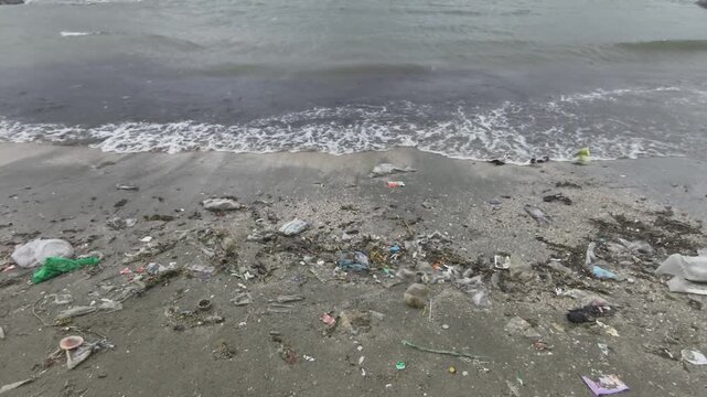 Sea waves washing plastic garbage and debris ashore on the beach during monsoon season.