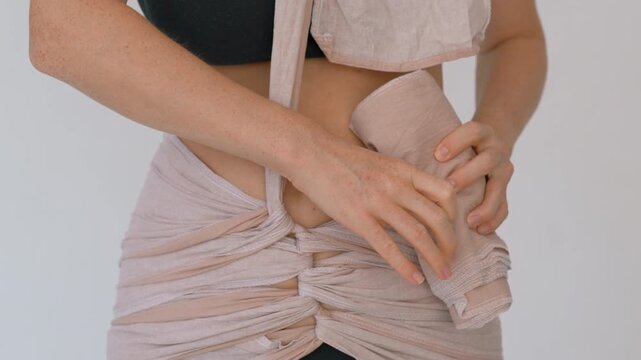 Woman tying bengkung belly wrap after childbirth. Close-up. Slow motion.