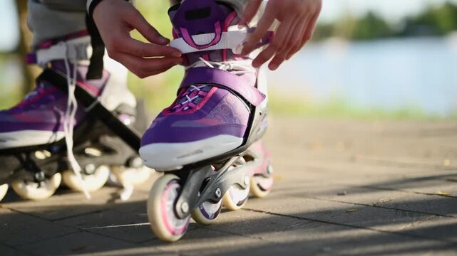 Teenager Hands buckle purple inline skates on a paved path near a lake during a sunny day Preparing for rollerblading