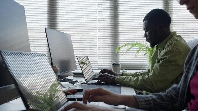 Rack focus shot of Multiethnic software developers typing on laptops in modern office. Perfect for technology startups, AI development agencies, and IT consulting corporate videos