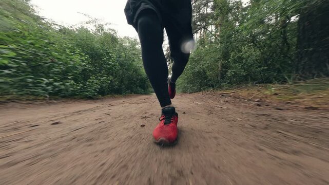 Man runs on a dirt path surrounded by trees during daytime in a forest location in slow motion