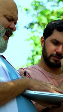 Indian doctor patient discuss case outdoors in natural greenery as senior male physician reviews medical report on laptop or looking at case file with patient during open air healthcare consultation