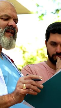 Indian doctor patient discuss case outdoors in natural greenery as senior male physician reviews medical report on laptop or looking at case file with patient during open air healthcare consultation