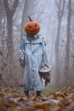Close view of a pumpkin headed monster holding a scarecrow head in autumn woodland. Halloween themed portrait with foggy background and haunting atmosphere