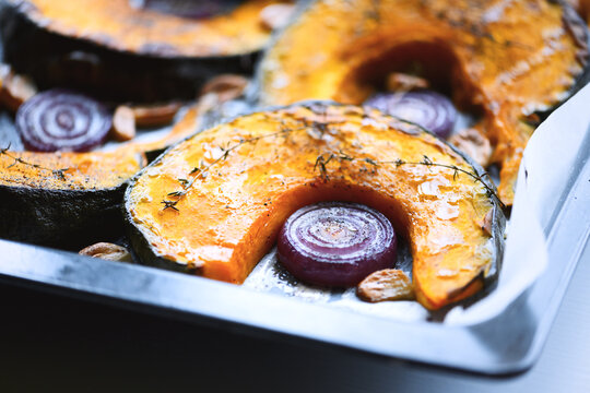 Baked pumpkin slices and red onion arranged in roasting pan. Seasonal comfort food with squash and rustic kitchen styling