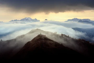 A lone hiker stands above a sea of clouds near Passo Giau at sunrise in the Dolomites. Dramatic mountain landscape with misty valleys, layered ridges and golden light © Ivan Kmit