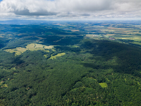 Aerial view of the lush green hills of Bohunicky Rohac in Stiavnicke Vrchy with dense forests and scattered fields under a cloudy sky in Bohunice, Nitra Region, Slovakia.