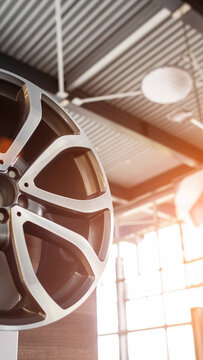 New alloy car wheel rim on display in modern auto dealership showroom, polished surface reflecting bright window light and warm sun flare, automotive luxury product vertical photo