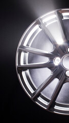 Obraz premium Close-up view of shiny metallic car wheel rim with bright reflections on spokes and polished surface against dark background, automotive part detail vertical photo