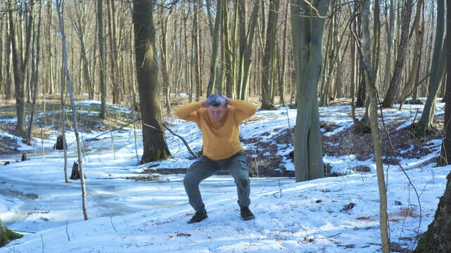Man performing bodyweight squats outdoors in snowy spring forest landscape, functional fitness workout promoting strength mobility and endurance