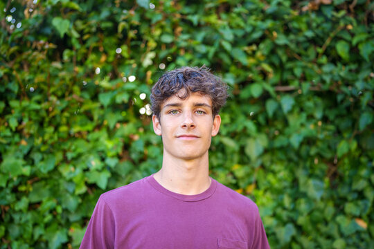 Young man posing outdoors, looking at camera with green background, capturing a natural moment