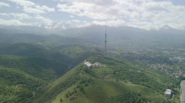 6.6.2026 Almaty.Kazakhstan. Aerial view of Kok Tobe TV tower on a green hill with Almaty city and mountains in the background, Kazakhstan