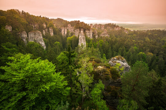 Rock city formations in Hruba Skala, Bohemian Paradise (Cesky raj), rising from forest seen from above. Orange sunrise sky lights sandstone towers and valleys panoramic view sky .