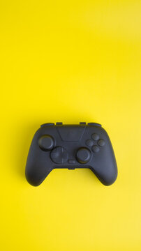 Vertical flat lay of blank black gamepad mockup on yellow background with negative space for gaming design.

