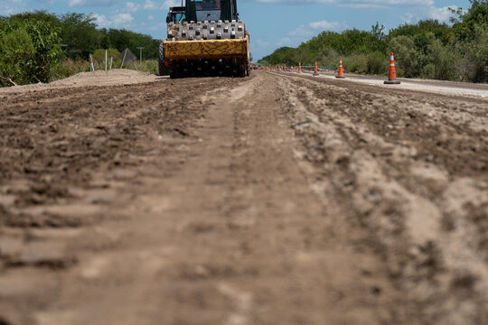Heavy padfoot soil compactor working on leveling and flattening a dirt road at a construction site.