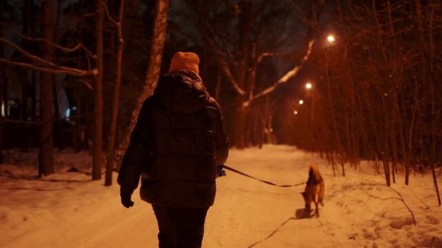 Woman walking her dog on a snowy street of a suburban area at night
