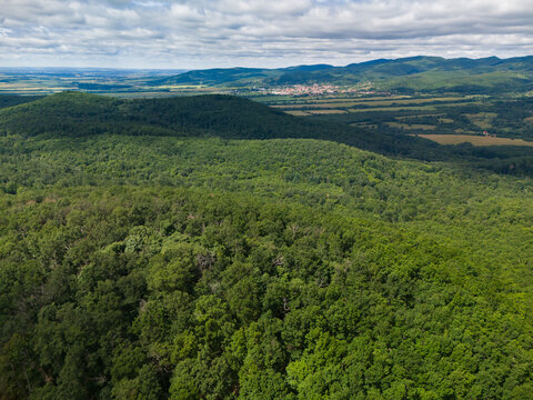 Aerial view of the lush green forests of Bohunicky Rohac in Stiavnicke Vrchy with rolling hills and a distant village under a cloudy sky Bohunice, Nitra Region, Slovakia.