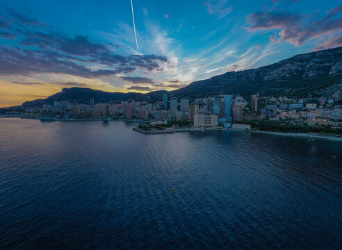 Aerial view of the Monte Carlo skyline at twilight with high-rise buildings along the Mediterranean coast and mountains under a colorful sky in Monaco, Monaco.