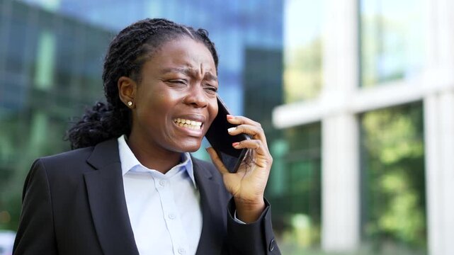 Angry African American businesswoman and boss yells while talking during a tense smartphone call in this close-up view. The furious female executive is aggressively scolding her subordinate on street.