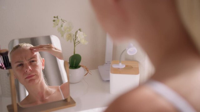 Concerned woman examining wrinkles in mirror and touching face, feeling insecure about aging and changes in facial appearance.Appearance concern, aging anxiety, emotional wellbeing concept