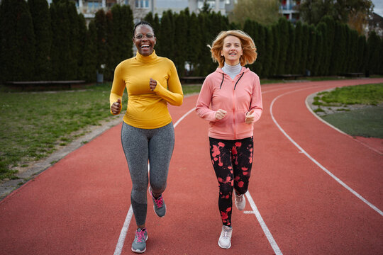 Diverse women friends running together on outdoor track