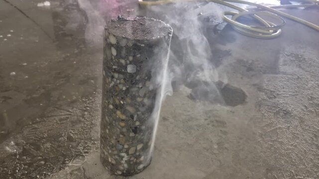 High frame rate footage of a hot concrete core sample with visible gravel and rebar, showing the steam slowly rising from the heated surface.