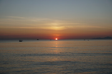 Fototapeta premium Red golden sun rises over the sea. Fishing boats in the sea with the sun setting in the background. Beautiful golden dawn