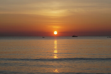 Fototapeta premium The red golden sun rises over the sea and fishing boats. Beautiful seascape at dawn. Bright sun rises over the horizon of the sea