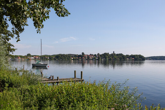 Peaceful landscape at Gro&szlig;er Pl&ouml;ner See, Germany, featuring a sailboat moored near a wooden pier on calm water under a clear blue sky. Ideal for travel stock.