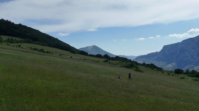 Un ampio prato verde ai piedi di colline e montagne, sotto un cielo limpido. Una scena naturale serena e panoramica