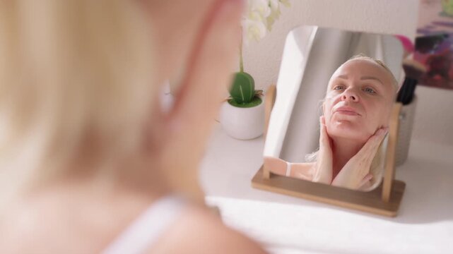 Woman applying moisturizing face cream and anti aging serum during morning skincare routine, look at mirror and caring for healthy glowing skin at home.Skincare routine, anti aging, self care concept