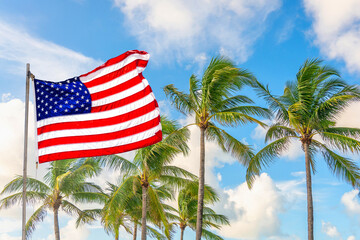 Fototapeta premium American flag waving against palm trees on blue sky background