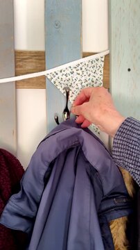 Vertical video social media - Closeup slow motion shot of a man&rsquo;s hand hanging a blue jacket from a hook on a basic rustic painted wooden clothes rack.