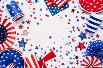 Obraz premium Fourth of July party supplies scattered on white surface with red blue white confetti.