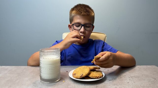 Young boy breaking a cookie at a kitchen table with a glass of milk