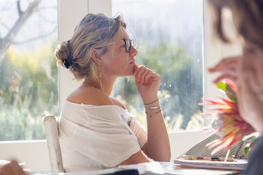 young woman at table, using mobile phone and thinking