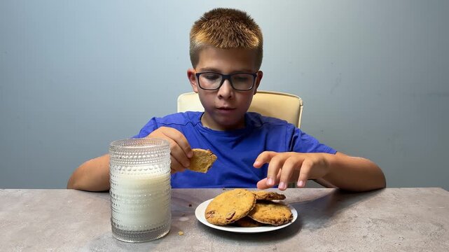 Young boy dunking a cookie into a glass of milk at a table