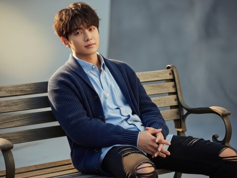 Portrait of a handsome young asian man sitting on a wooden bench outdoors