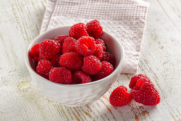 Fresh red raspberries in white ceramic bowl on wooden table with napkin © Andrei Starostin