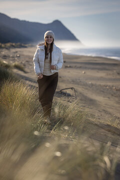 Woman stands on a sand dune in Gold Beach Oregon, dressed warmly. Smiling and enjoying the beautiful landscape in southern Oregon.