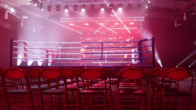 Empty boxing ring with rows of red chairs under dramatic stage lighting at arena