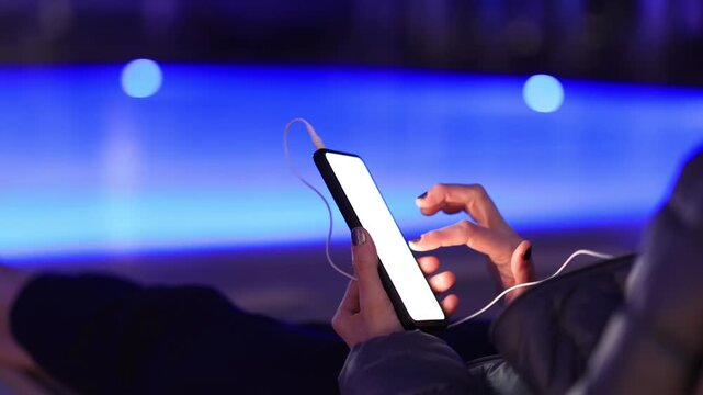 Woman using smartphone by pool at night &ndash; glowing screen, copy space, modern lifestyle.