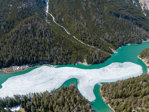 Aerial view of the partially frozen turquoise waters of Lai da Ova Spin near Fuorn Pass surrounded by dense evergreen forests on mountain slopes in Val Mustair, Grisons, Switzerland.