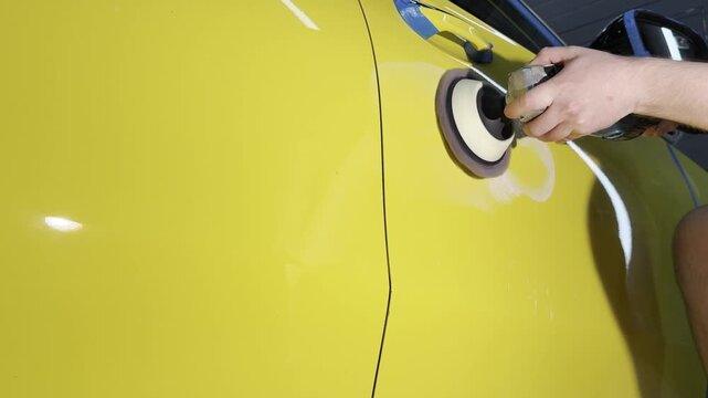 A car service worker polishes the yellow car body with a polishing machine. Detailing and polishing of the car. Car detailing - hands with an orbital polishing machine in an auto repair shop. PDR. 