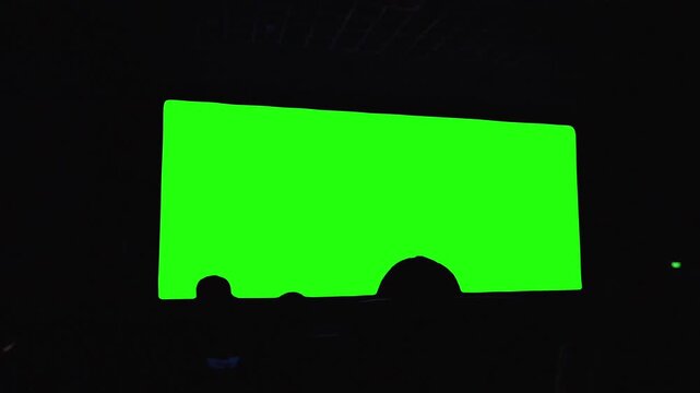 Large cinema screen mockup featuring chroma key green screen with audience silhouettes in foreground, ideal for custom video insertion, film promotion, advertising campaigns and media presentations