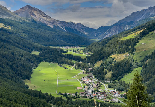 Aerial view of the lush green valley near Fuorn Pass with a small alpine village surrounded by dense pine forests and rugged mountain peaks Val Mustair, Grisons, Switzerland.