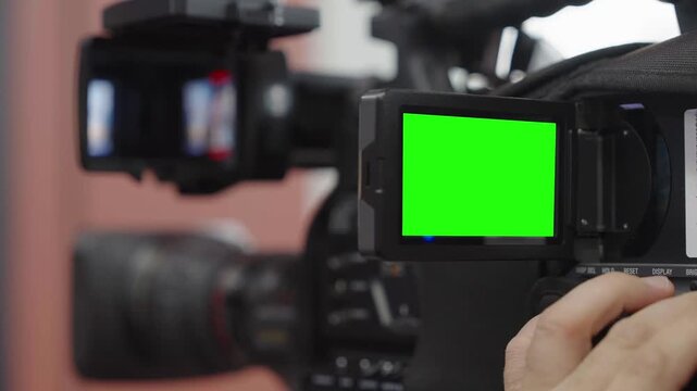 Broadcast camera operator preparing equipment for television coverage with chroma key green screen visible on display. Concept of news production, live transmission, journalism, media technology
