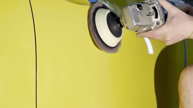 A car service worker polishes the yellow car body with a polishing machine. Detailing and polishing of the car. Car detailing - hands with an orbital polishing machine in an auto repair shop. PDR. 